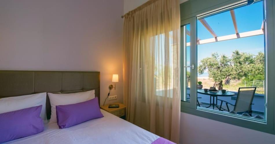 a bedroom with a bed with purple pillows and a balcony at Terra di Olive Thassos in Potos