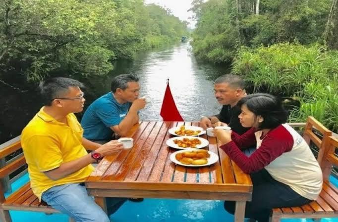 a group of people sitting at a picnic table by a river at Cakrawala in Kumai