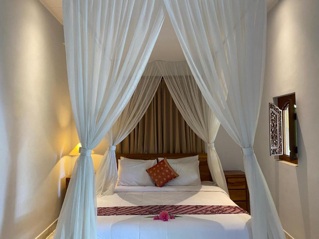 a bedroom with a canopy bed with white curtains at Aura Bisma Guesthouse in Ubud
