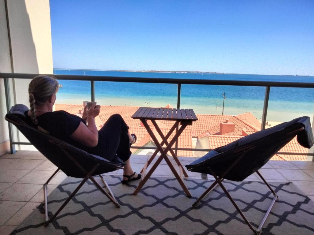 eine Frau auf einem Stuhl auf einem Balkon mit Blick auf den Strand in der Unterkunft The Boardwalk Apartment in Rockingham