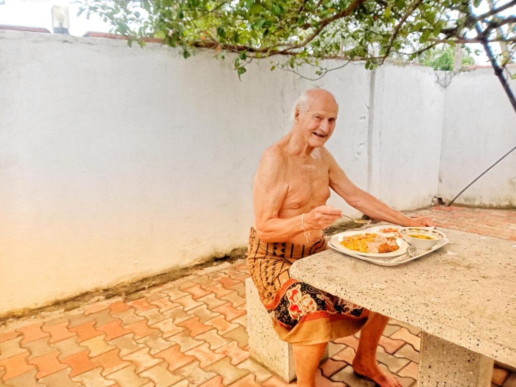 Un uomo anziano seduto a un tavolo con un piatto di cibo di Royal Princess Holiday Inn a Alutgama