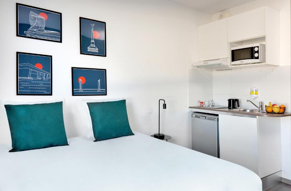 a white bedroom with a bed and a kitchen at Ténéo Apparthôtel Bordeaux Maritime - Cité du vin in Bordeaux