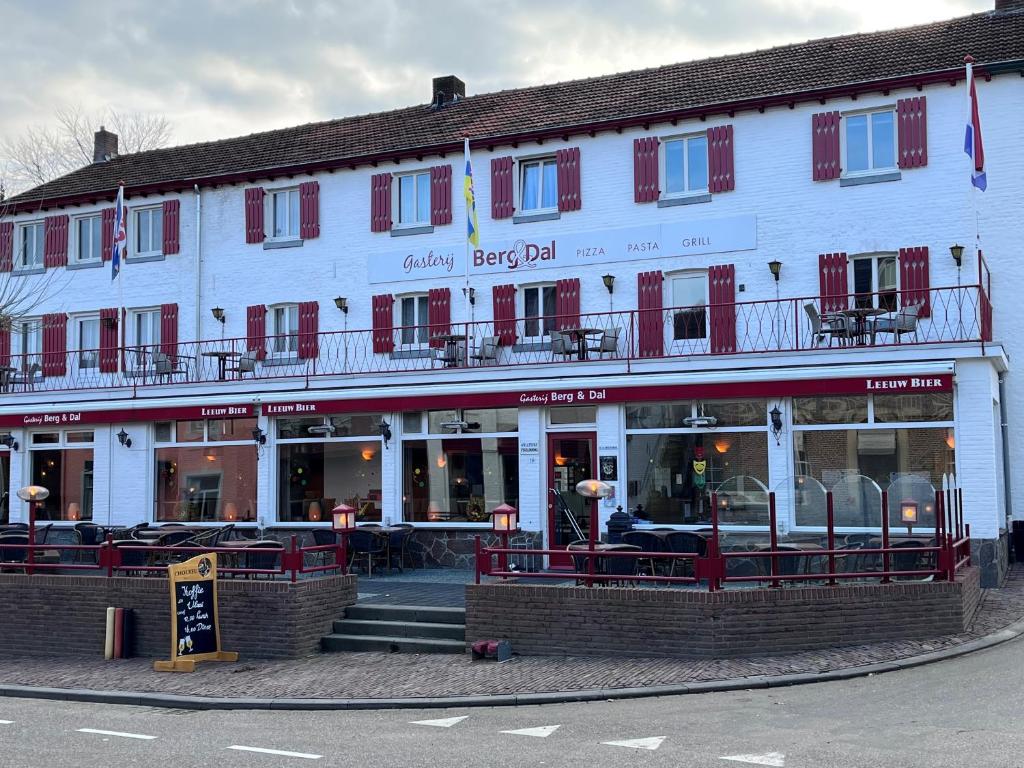un grand bâtiment blanc avec volets rouges dans une rue dans l'établissement Gasterij Berg en Dal, à Slenaken