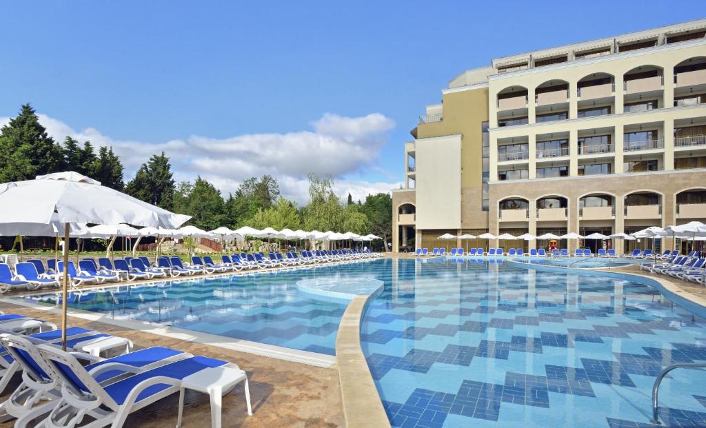 a large swimming pool with blue chairs and a building at Sol Nessebar Bay All Inclusive in Nesebar