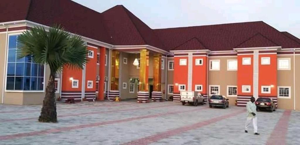 um homem a andar em frente a um edifício com uma palmeira em Joclarif Hotel and Suites em Zaria