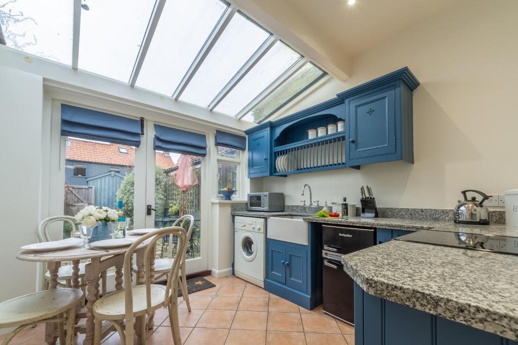 Bracken Cottage في برانكاستير: مطبخ مع دواليب زرقاء وطاولة وكراسي