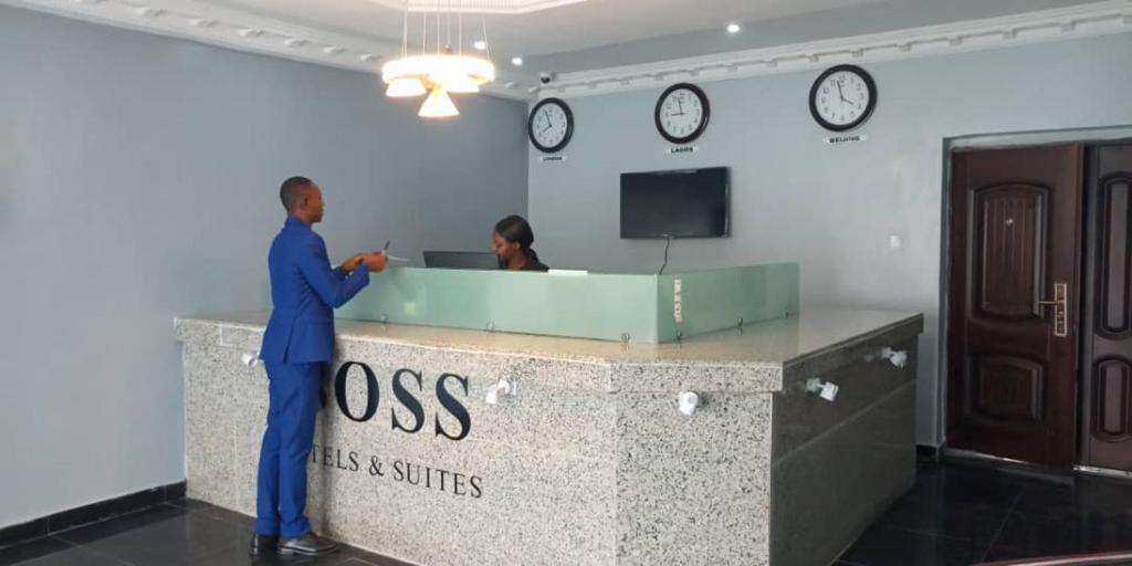 Ein Mann steht an einem Schreibtisch in einem Büro mit zwei Uhren. in der Unterkunft BOSS HOTELS & SUITES in Lagos
