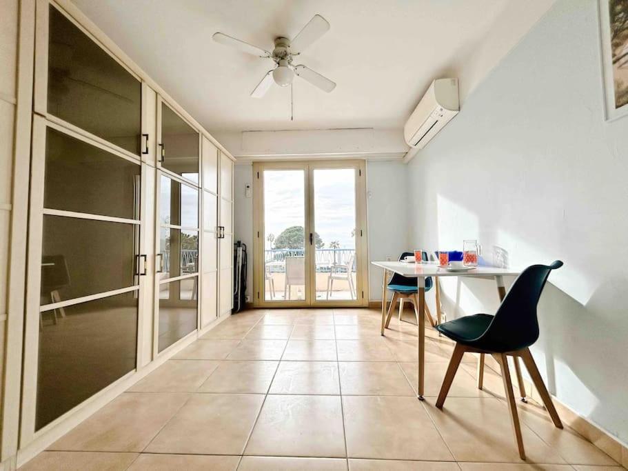 Le Dulys : Apt 2 prs, vue mer, clim, 2 min plages في أنتيب: غرفة معيشة مع طاولة وكراسي ومروحة سقف