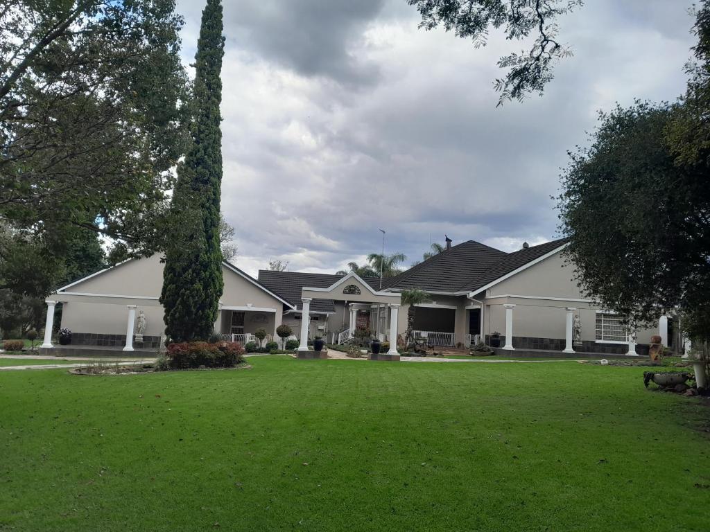 a large white house with a green yard at Longtom Farm Guesthouse in Lydenburg