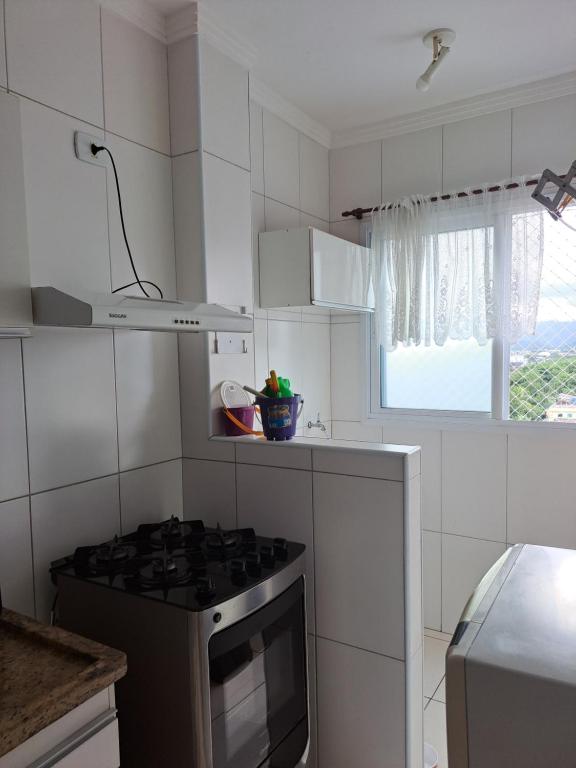 a white kitchen with a stove and a window at Apto aconchegante beira mar com ar no quarto in Solemar