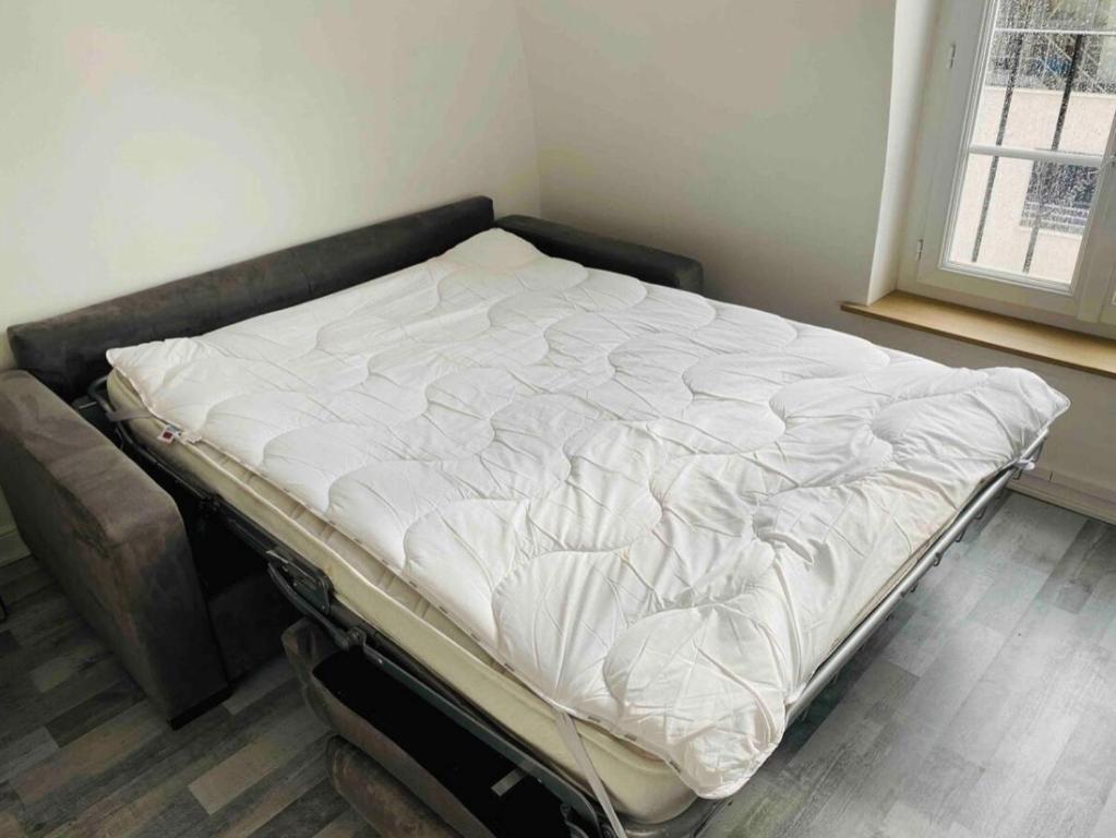 ein unmaskiertes Bett in einem Zimmer neben einem Fenster in der Unterkunft Studio Paris centre tout équipé in Paris