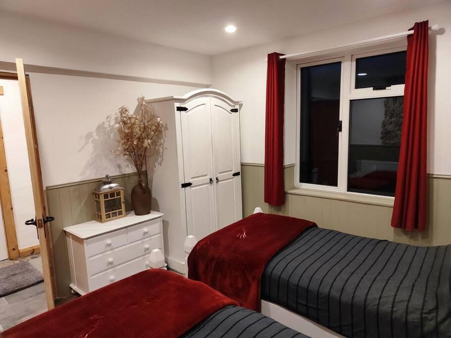 a bedroom with two beds and a window with red curtains at Kempies-Cozy house on the NC500 in Durness