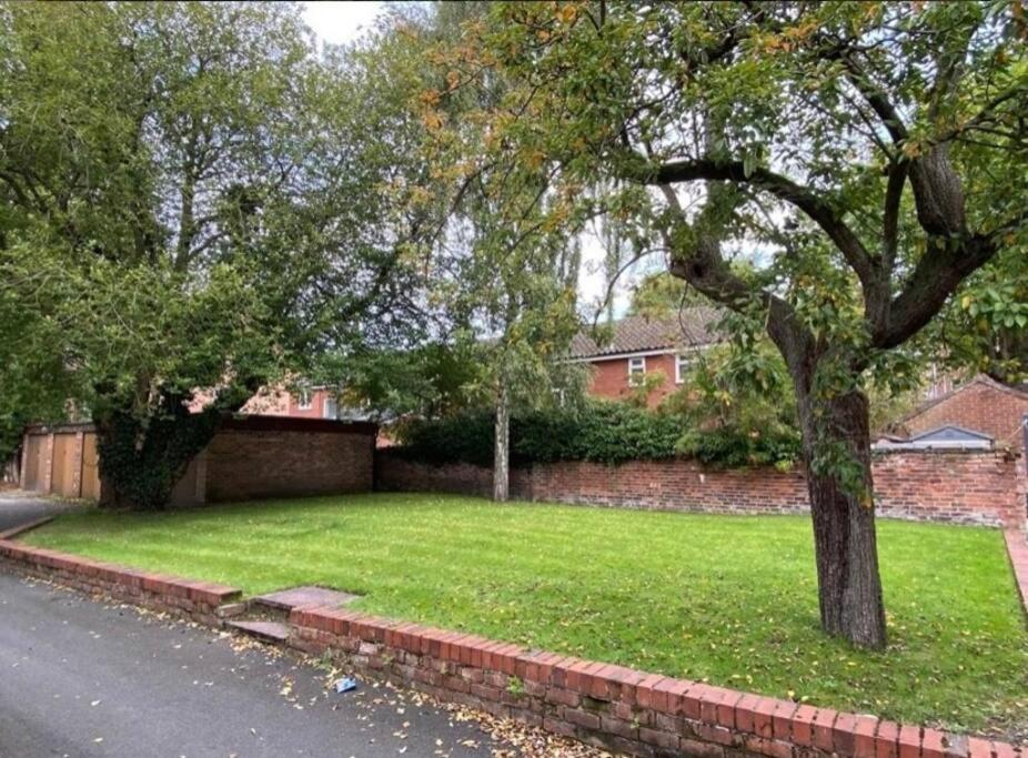 a green yard with a tree and a brick wall at DIDSBURY Fáilte Inn Apts - 3 Mins to The Christie's - Ground Floor - FREE Parking in Manchester