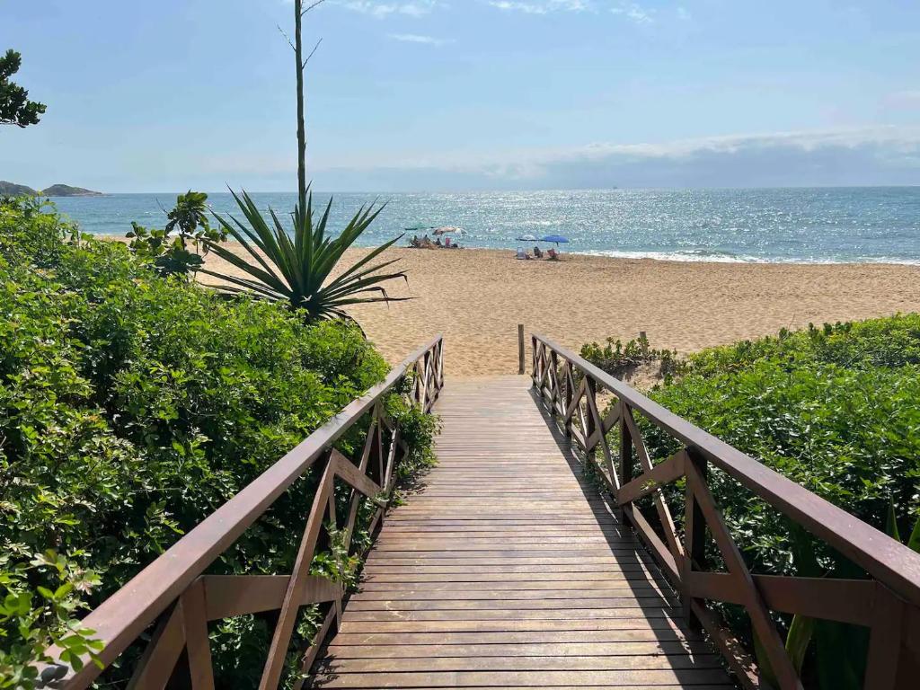 een houten promenade die leidt naar een strand met de oceaan bij Casa pé na areia em praia paradisíaca com piscina frente mar in Balneário Camboriú