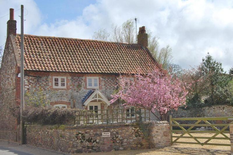 a stone house with a fence and a flowering tree at Mayes Cottage in Brancaster