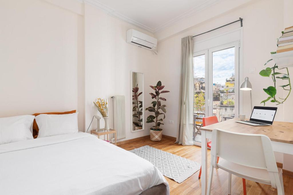ein weißes Schlafzimmer mit einem Bett und einem Schreibtisch mit einem Laptop in der Unterkunft Studio with sunny balcony in Exarcheia in Athen