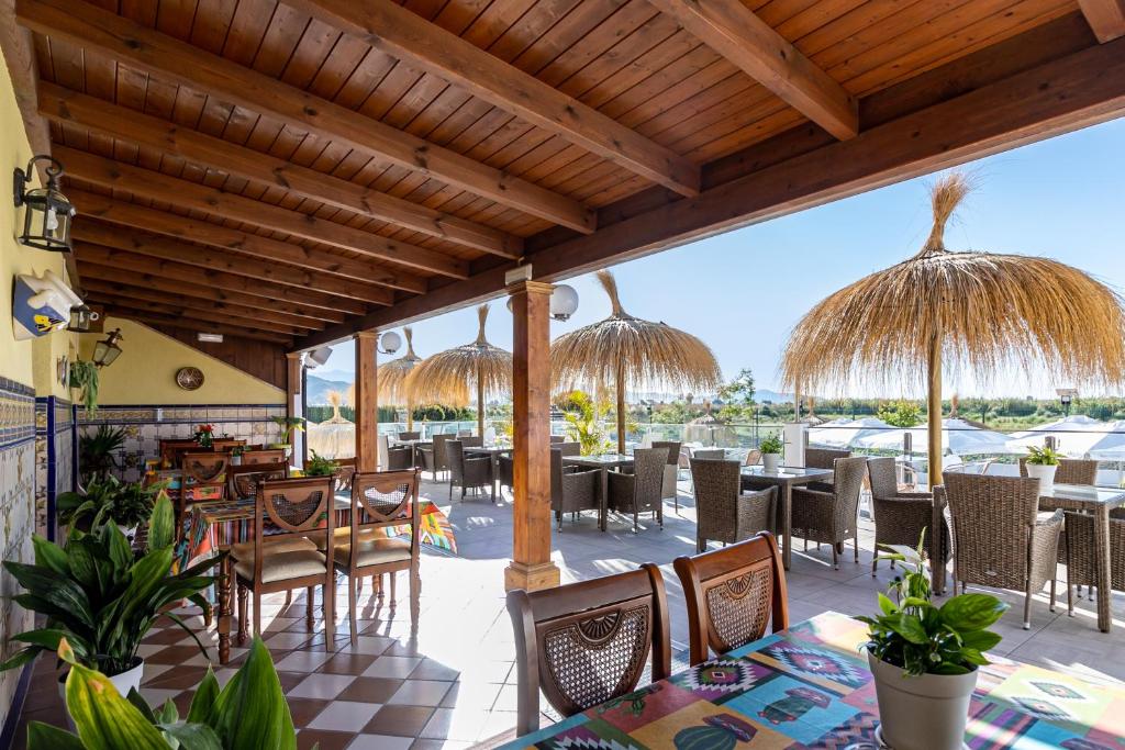 ein Restaurant mit Tischen, Stühlen und Strohschirmen in der Unterkunft Hotel Avenida Tropical by Bossh! Hotels in Salobreña