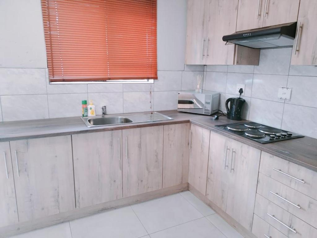 a kitchen with wooden cabinets and a sink and a microwave at Reutlwane Gardens Guesthouse in Secunda