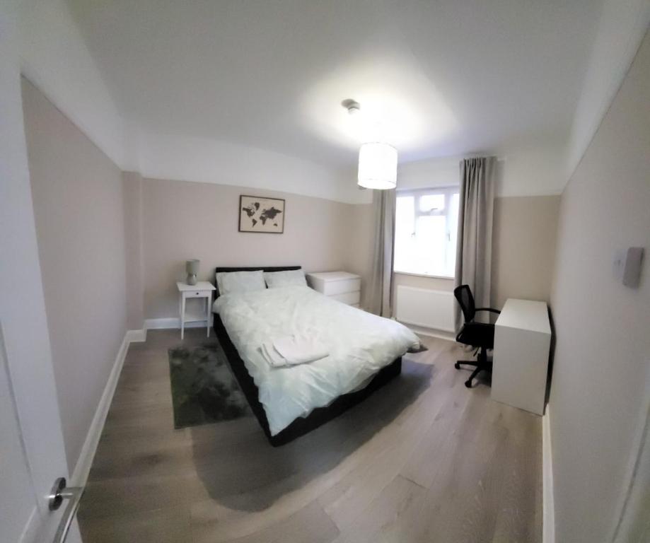 a white bedroom with a bed and a desk at Warm cosy family home in East Tilbury