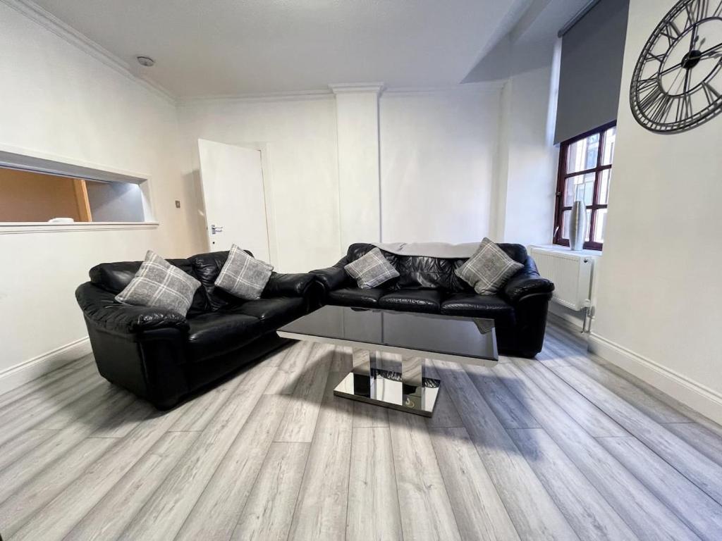 a living room with a black leather couch and a clock at Recently Refurbished Two Bedroom Apartment, Central Location! in Glasgow