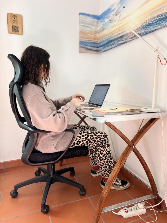 a woman sitting in a chair at a desk with a laptop at Hostel Nature in Zambujeira do Mar
