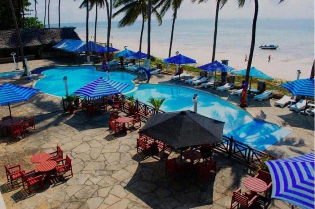 una grande piscina con tavoli, sedie e ombrelloni blu di Sai Rock Beach Hotel & Spa a Bamburi