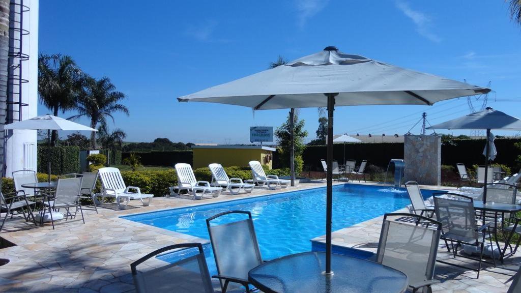 a pool with chairs and a table with an umbrella at Hotel Green Village in Jardinópolis