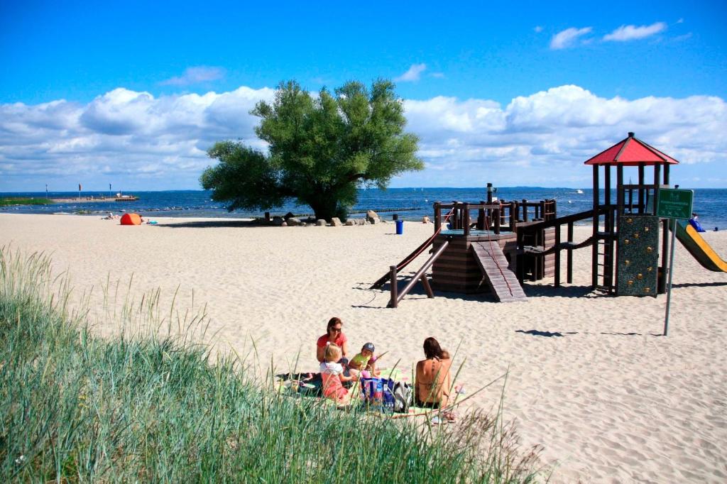 two women and a child sitting on a beach with a playground at waldhaus no 15 in Mönkebude