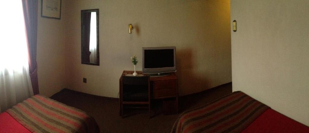 a room with two beds and a television on a table at Hotel Mercurio in Punta Arenas