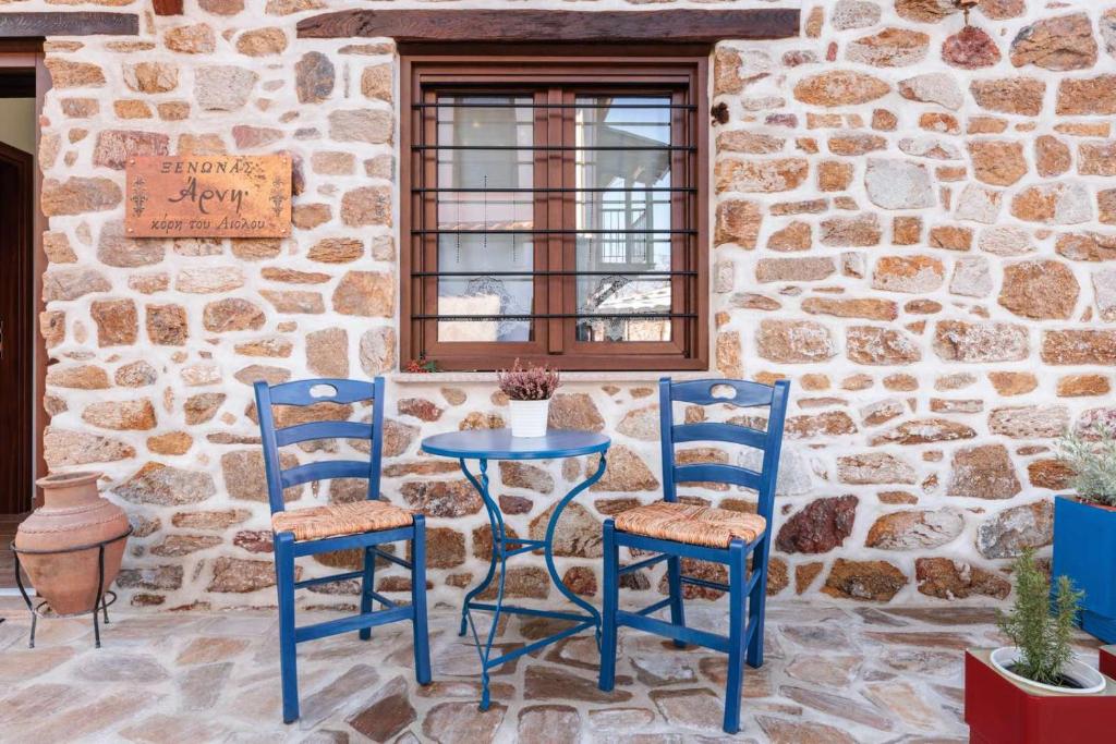une table bleue et deux chaises assises à côté d'un mur en pierre dans l'établissement Άρνη' κόρη του Αιόλου 2, à Arnaia