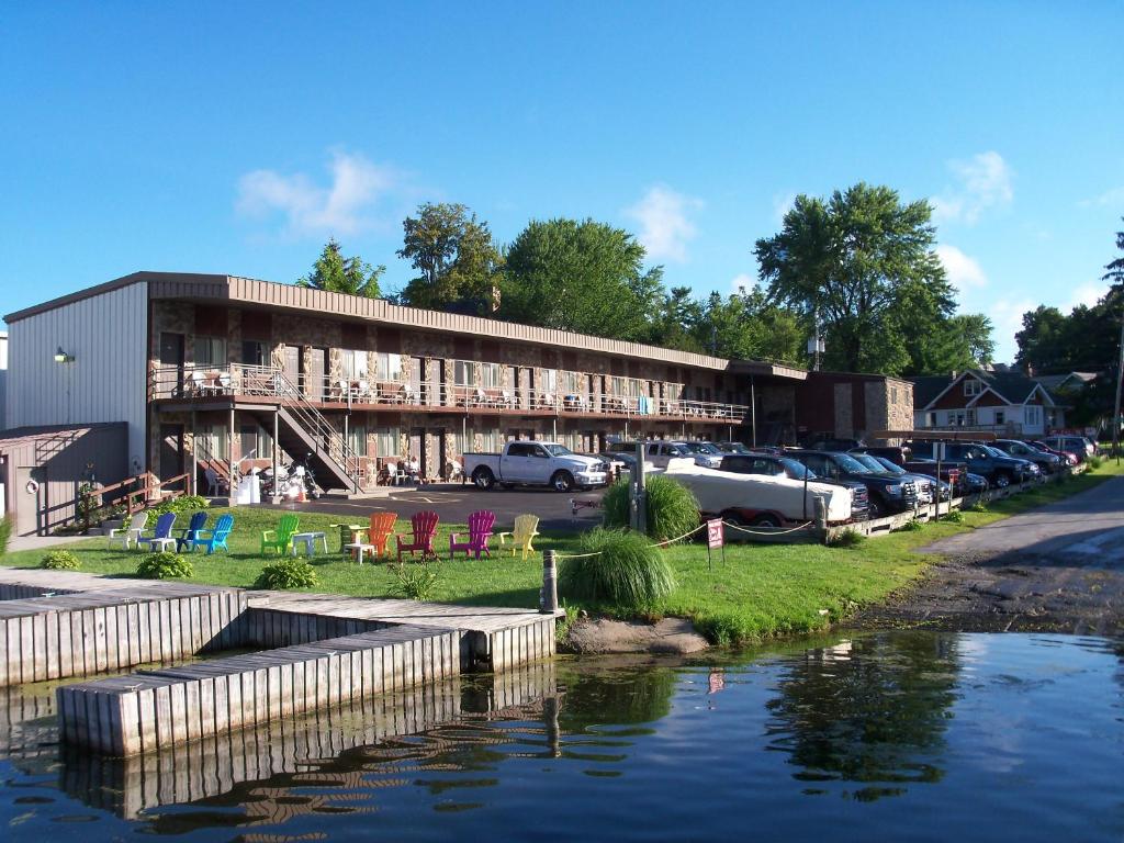 a building with cars parked in a parking lot next to a river at Otter Creek Inn in Alexandria Bay