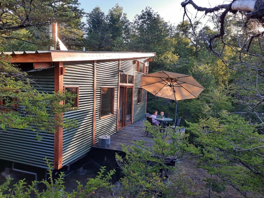 ein Haus mit einer Terrasse mit einem Tisch und einem Sonnenschirm in der Unterkunft Cabaña entre Bosque y Cordillera in Lonquimay