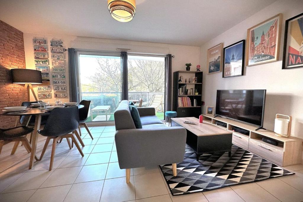 sala de estar con TV, mesa y sillas en L'Odyssée-Appart au calme avec balcon et parking en Nantes