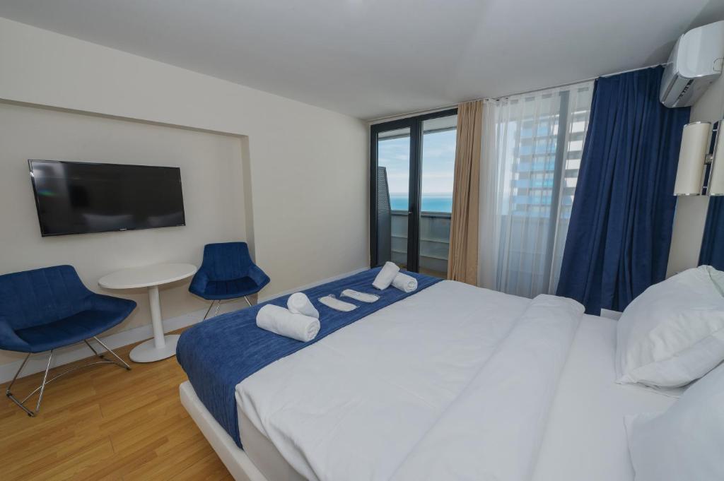 a bedroom with a large bed with blue chairs and a tv at Twin Towers Orbi City Batumi in Batumi