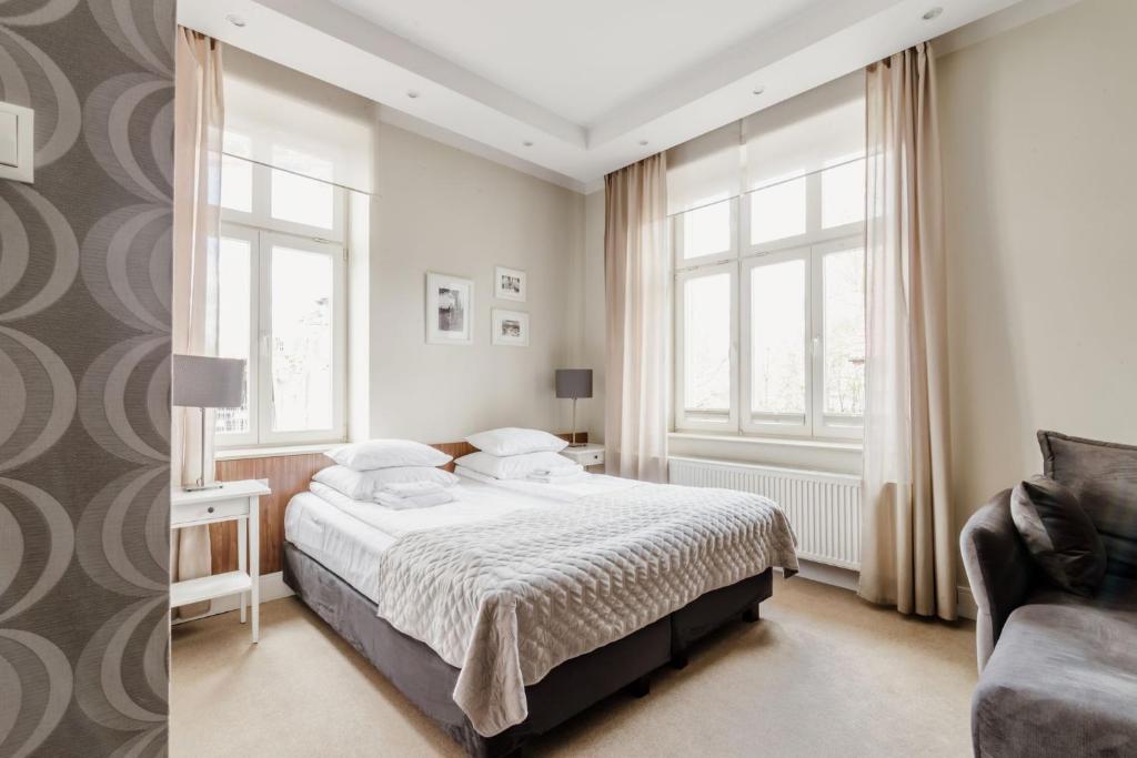 a white bedroom with a bed and a chair at Villa Baltica Gdańsk in Gdańsk