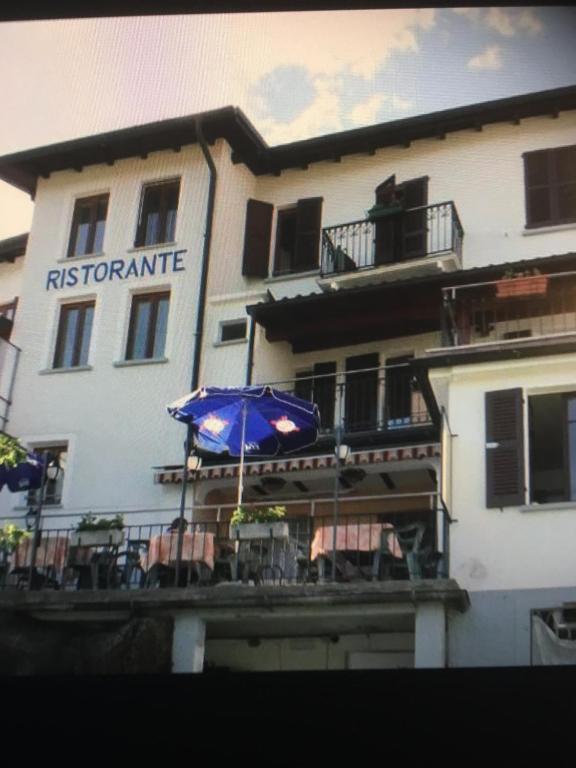 a building with an umbrella and chairs in front of it at Ristorante Bar Pensione Novaggio in Novaggio