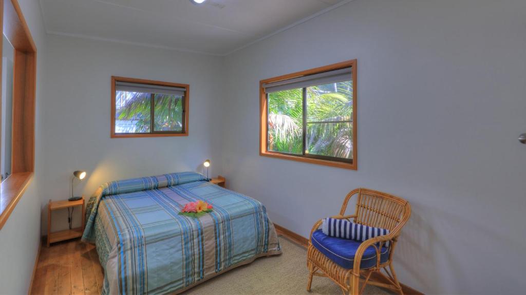 a bedroom with a bed and a chair and two windows at Somerset Apartments in Lord Howe