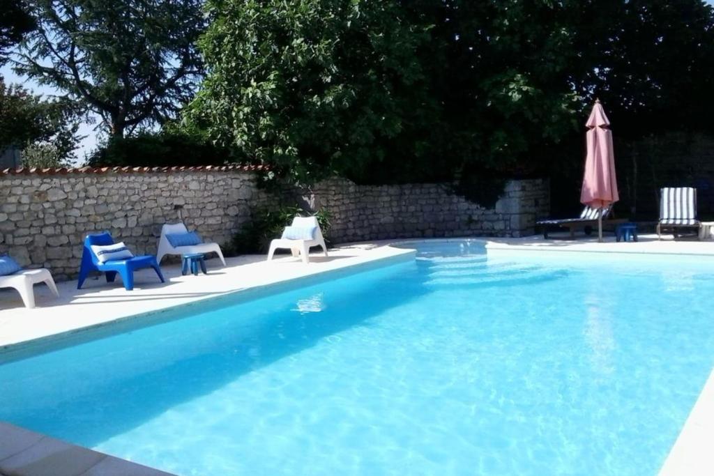 einen Pool mit blauen Stühlen und einem Sonnenschirm in der Unterkunft "Le Petit Breuil" near Saintes in Les Essards