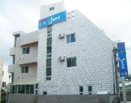 een wit bakstenen gebouw met een blauw bord erop bij Jun Motel in Jeju-stad