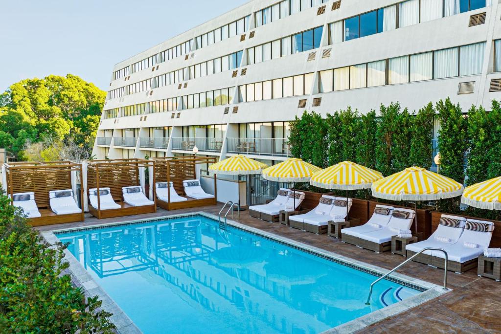 a swimming pool with chairs and umbrellas next to a building at Hotel Dena, Pasadena Los Angeles, a Tribute Portfolio Hotel in Pasadena