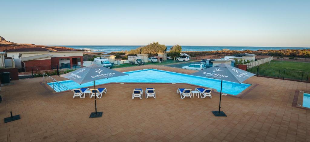an overhead view of a swimming pool with umbrellas and chairs at Kalbarri Red Bluff Tourist Park in Kalbarri