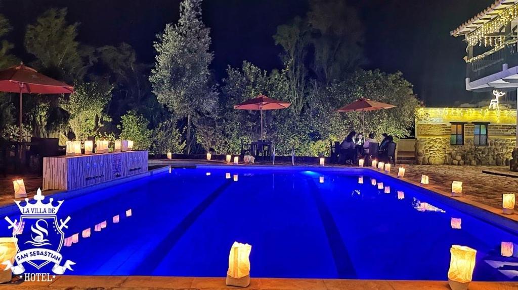 una gran piscina azul por la noche con sombrillas en La Villa de San Sebastian Hotel, en Villa de Leyva