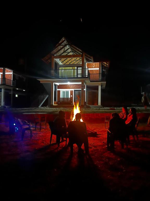 um grupo de pessoas sentadas à volta de uma fogueira à noite em Coorg Coffee Inn em Suntikoppa