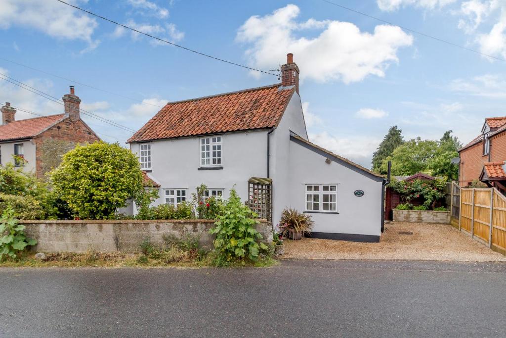 a white house with a red roof on a street at Hollyhedge Cottage in Briston