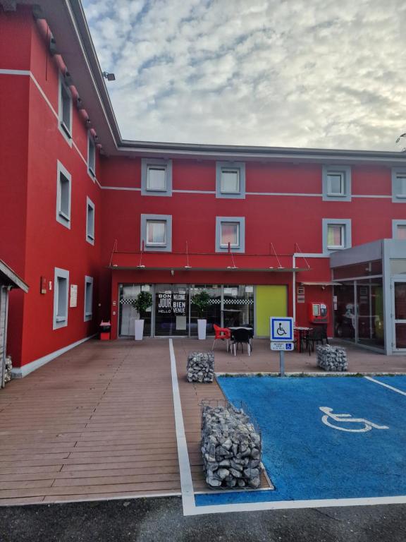 a red building with a lot of firewood in the courtyard at Enzo Hotels Reims Tinqueux by Kyriad Direct in Reims