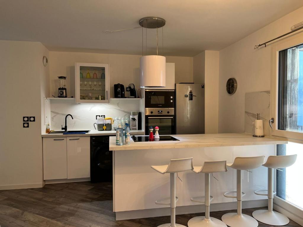 a kitchen with white cabinets and a counter with bar stools at Cosy T2 au porte d’Orly-Rungis in Chevilly-Larue
