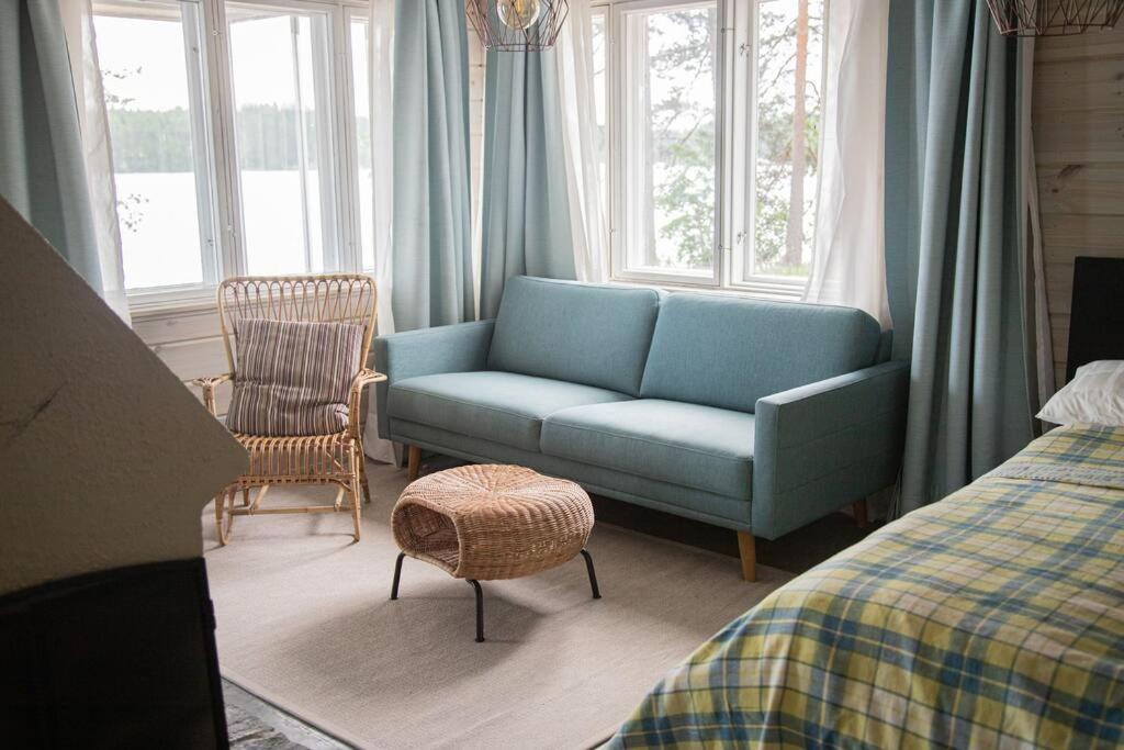 1 dormitorio con sofá, silla y ventanas en Ihana järvenranta mökki. Cottage by the lake., en Kurjalanranta