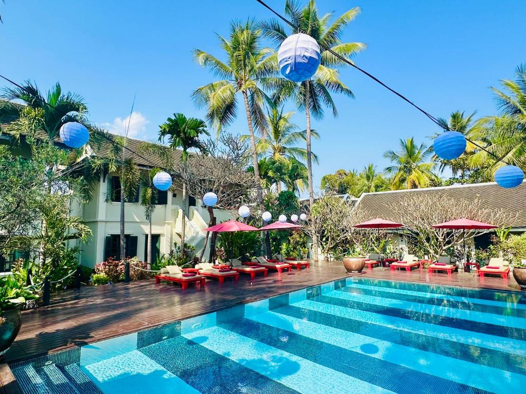 einen Pool in einem Resort mit Palmen und Sonnenschirmen in der Unterkunft Villa Maly Boutique Hotel in Luang Prabang