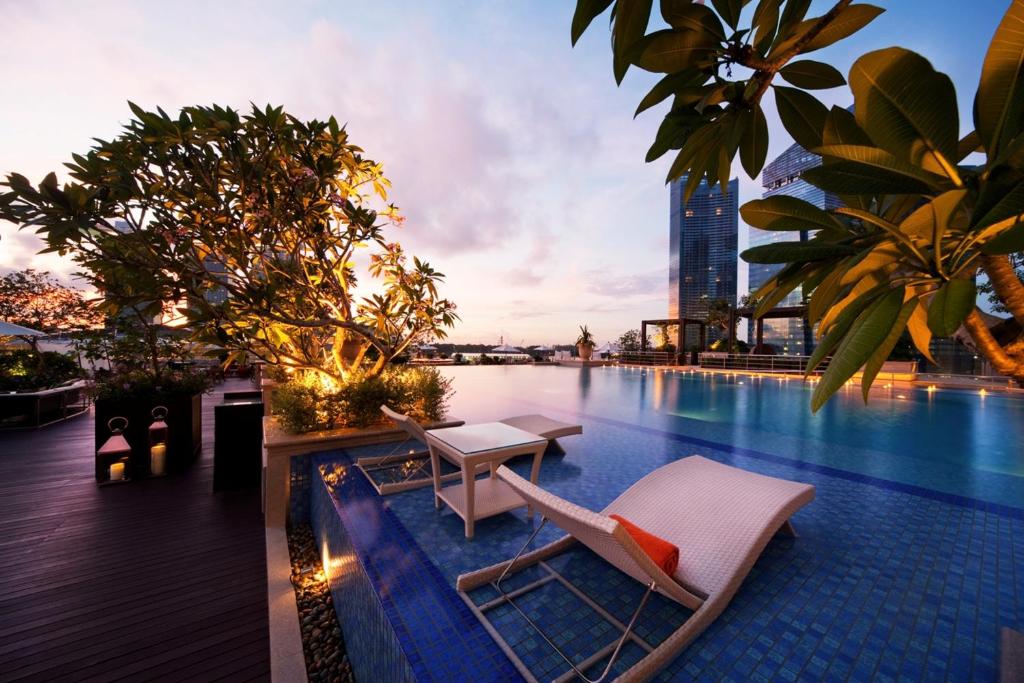 a swimming pool with two lounge chairs and a table at The Fullerton Bay Hotel Singapore in Singapore