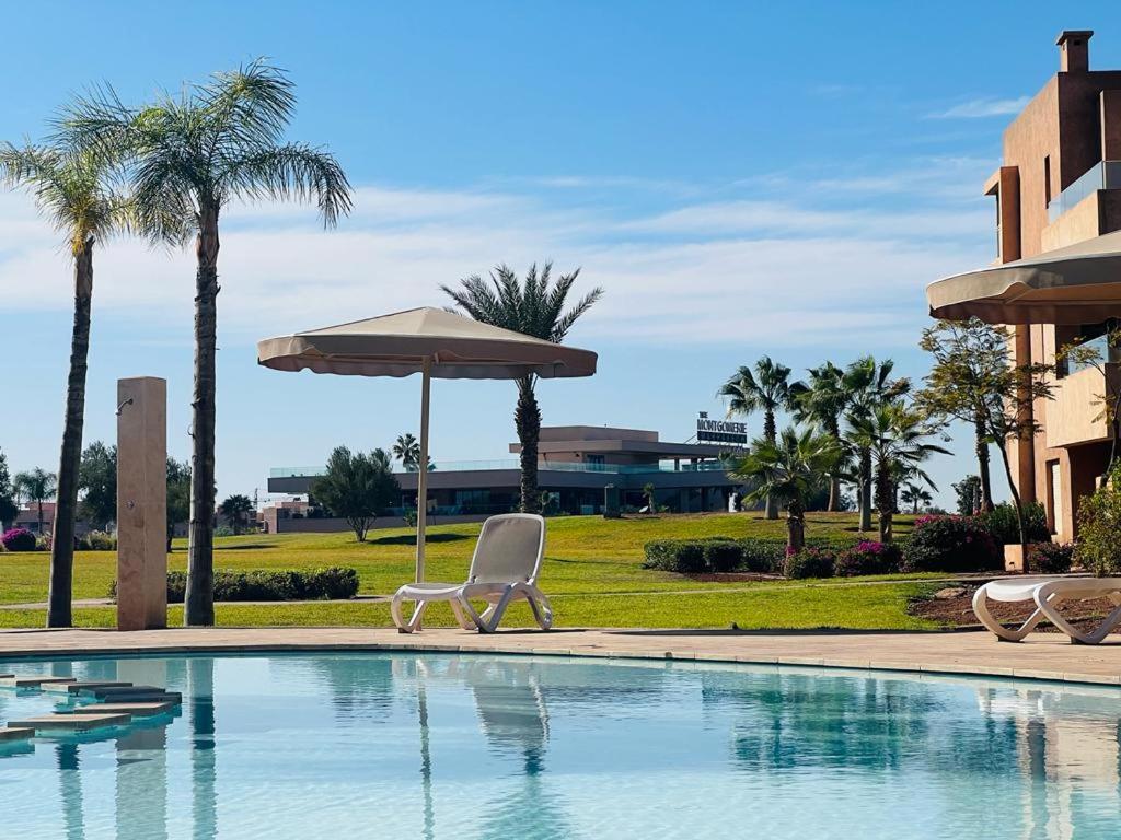 a pool with a chair and an umbrella and palm trees at Prestigia marrakech in Marrakech